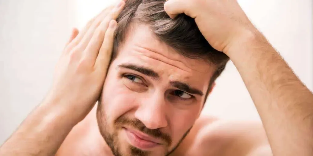 A man holding his head with thick hair.